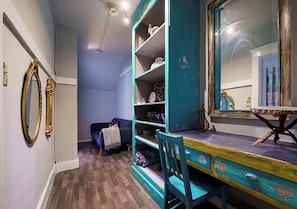 A room with a wooden floor, a teal-colored desk with drawers, a chair, and a large mirror.