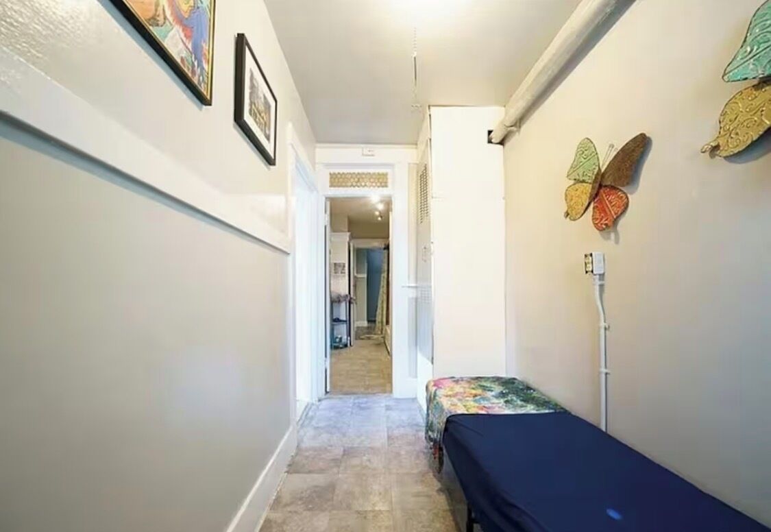 A narrow hallway with a bed on the right, a door at the end, and butterfly wall art.