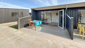 Un patio moderno al aire libre con terraza de madera, una mesa con sillas y un ventanal que da a un espacio interior.