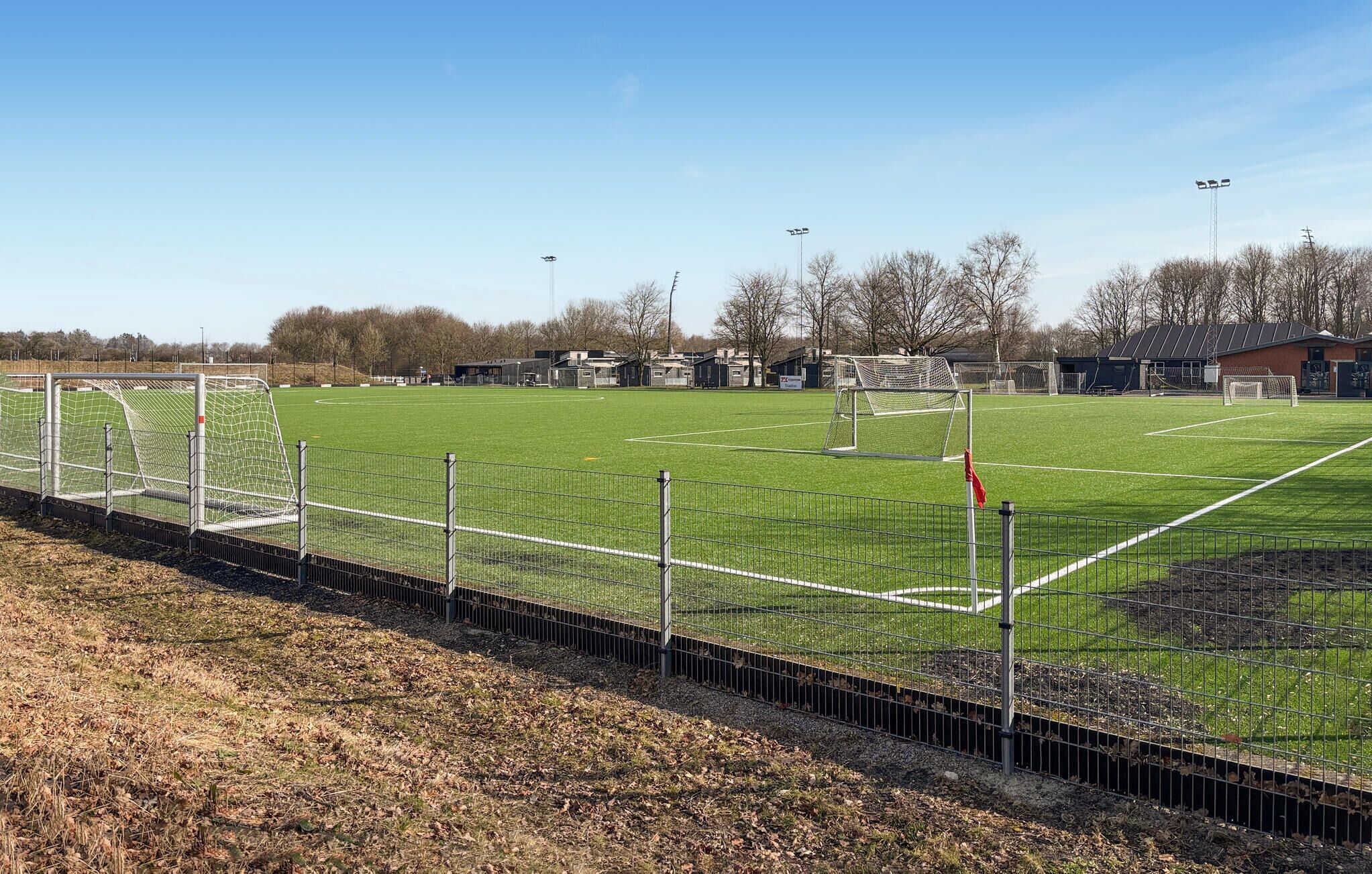 Un campo de fútbol con postes de portería, una valla y edificios al fondo.