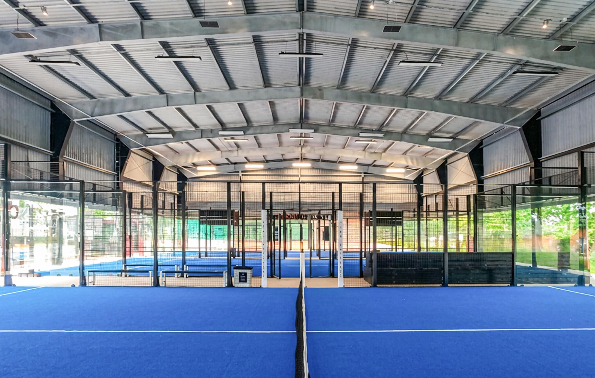 An indoor sports facility with a blue floor, metal roof, and glass walls.