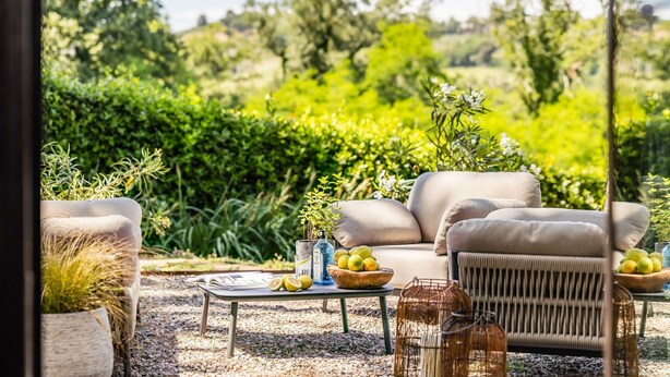 Eine Terrasse mit Gartenmöbeln, einem Tisch mit Büchern und Zitronen sowie einem Korbstuhl.