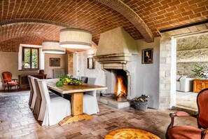 Ein rustikales Interieur mit Ziegeldecke, Kamin, Esstisch und Blick ins Freie.