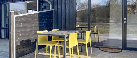 Un espace extérieur moderne aménagé avec une table et des chaises, une terrasse en bois et une porte vitrée donnant sur un paysage extérieur.