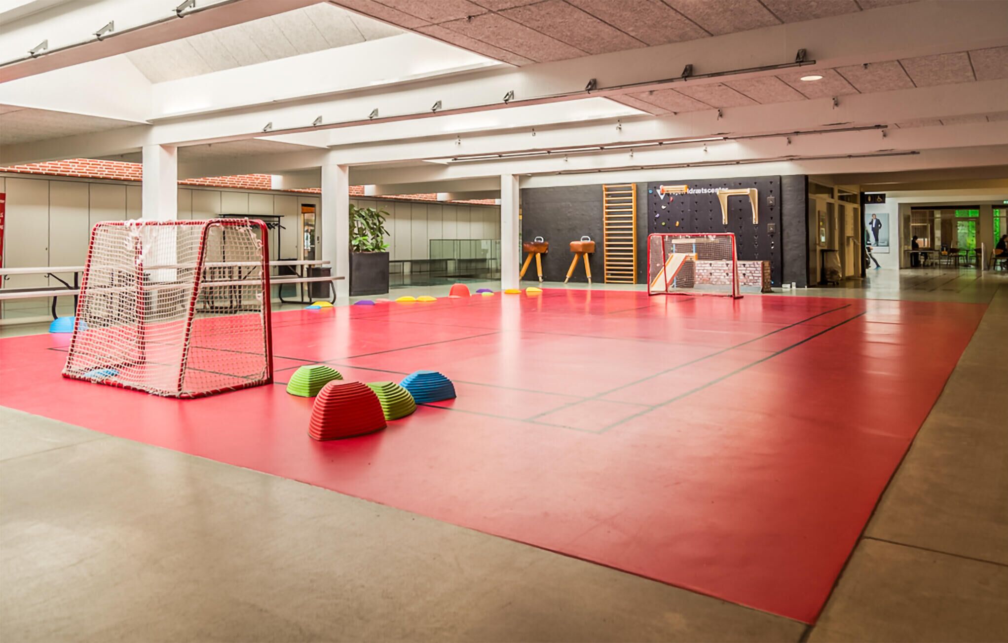 Instalación deportiva interior con suelo rojo, un arco y equipo de entrenamiento colorido.