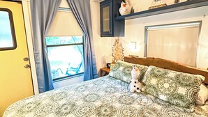 Un dormitorio con colcha estampada, un pequeño árbol decorativo y una estantería con una figura de muñeco de nieve.