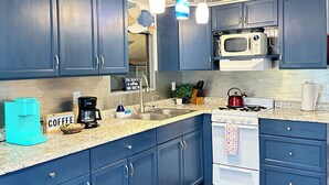 Una cocina con armarios azules, microondas, estufa, cafetera y luces colgantes.