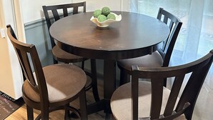 Un comedor con una mesa redonda, seis sillas y un bol de objetos verdes y esféricos. Dos cuadros están colgados en la pared, y recortes de Mickey Mouse se encuentran sobre el interruptor de la luz.