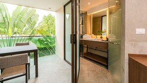 Een moderne badkamer met een douchecabine van glas, een wastafel met spiegel en uitzicht op weelderige begroeiing.