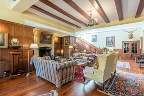 A spacious living room with wooden paneling, a fireplace, a staircase, and a mounted deer head. - Baronial Mansion - Five Bedroom Villa, Sleeps 10 (Alness)