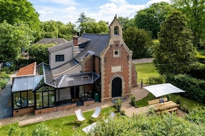 A house with a glass conservatory, a brick tower, and a lawn with outdoor seating.