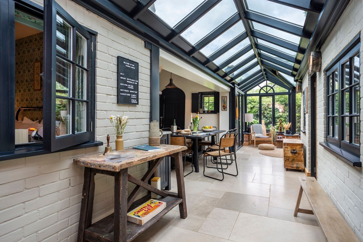 A conservatory with a glass roof, wooden furniture, and a brick wall.