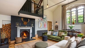 Una sala de estar con chimenea, un sofá verde, piso de madera y una escalera.