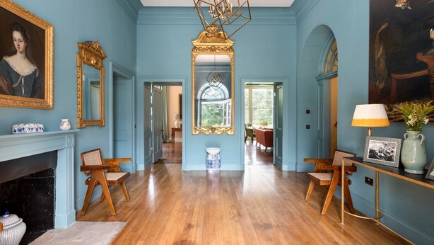 Ein Zimmer mit blauer Wand, Kamin, einer Chandelierleuchtre und einem großen Spiegel.