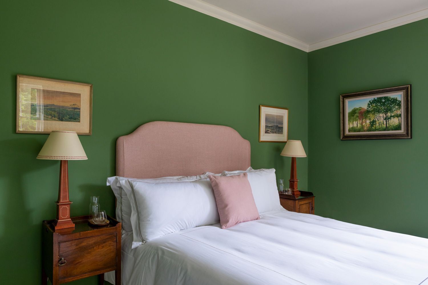A bedroom with a bed, two nightstands, two lamps, and three framed pictures on the walls.