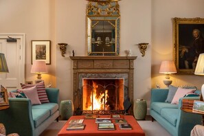 A living room with a fireplace, two sofas, a coffee table with books, and decorative lamps. - Nuthatch House - Eleven Bedroom Villa, Sleeps 24 (Thornhill)