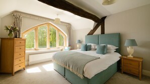 A bedroom with a large bed, a wooden dresser, a nightstand, a window with curtains, and a wooden beam ceiling. - Abbeville Barn - Four Bedroom Villa, Sleeps 11 (Langford)