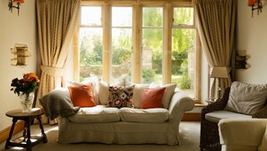 A cozy living room with a sofa, a side table with a vase, and a view of greenery through large windows. - Abbeville Barn - Four Bedroom Villa, Sleeps 11 (Langford)