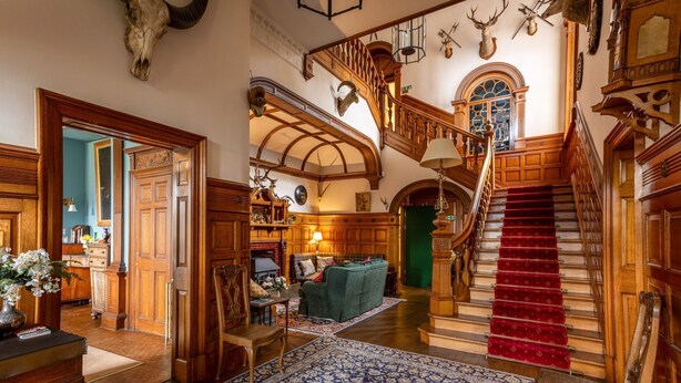 A grand hall with a staircase, wooden furniture, and mounted animal heads.