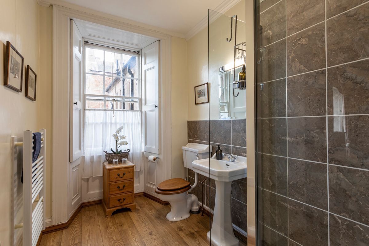 Un bagno con pavimento in legno, un water bianco, un lavabo su piedistallo e una doccia con piastrelle scure.