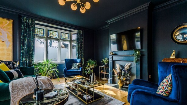 A living room with a fireplace, blue armchairs, a coffee table, and a large window with curtains.