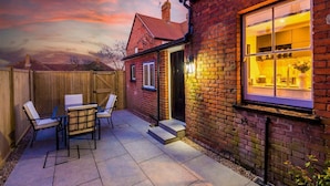 A brick house with a patio, a table with chairs, and a window with interior lighting.