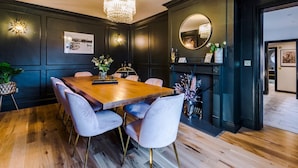A dining room with a wooden table and chairs, a chandelier, wall-mounted lights, and a fireplace.