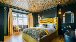 A room with a large bed, a chair, a radiator, and a window with curtains.
