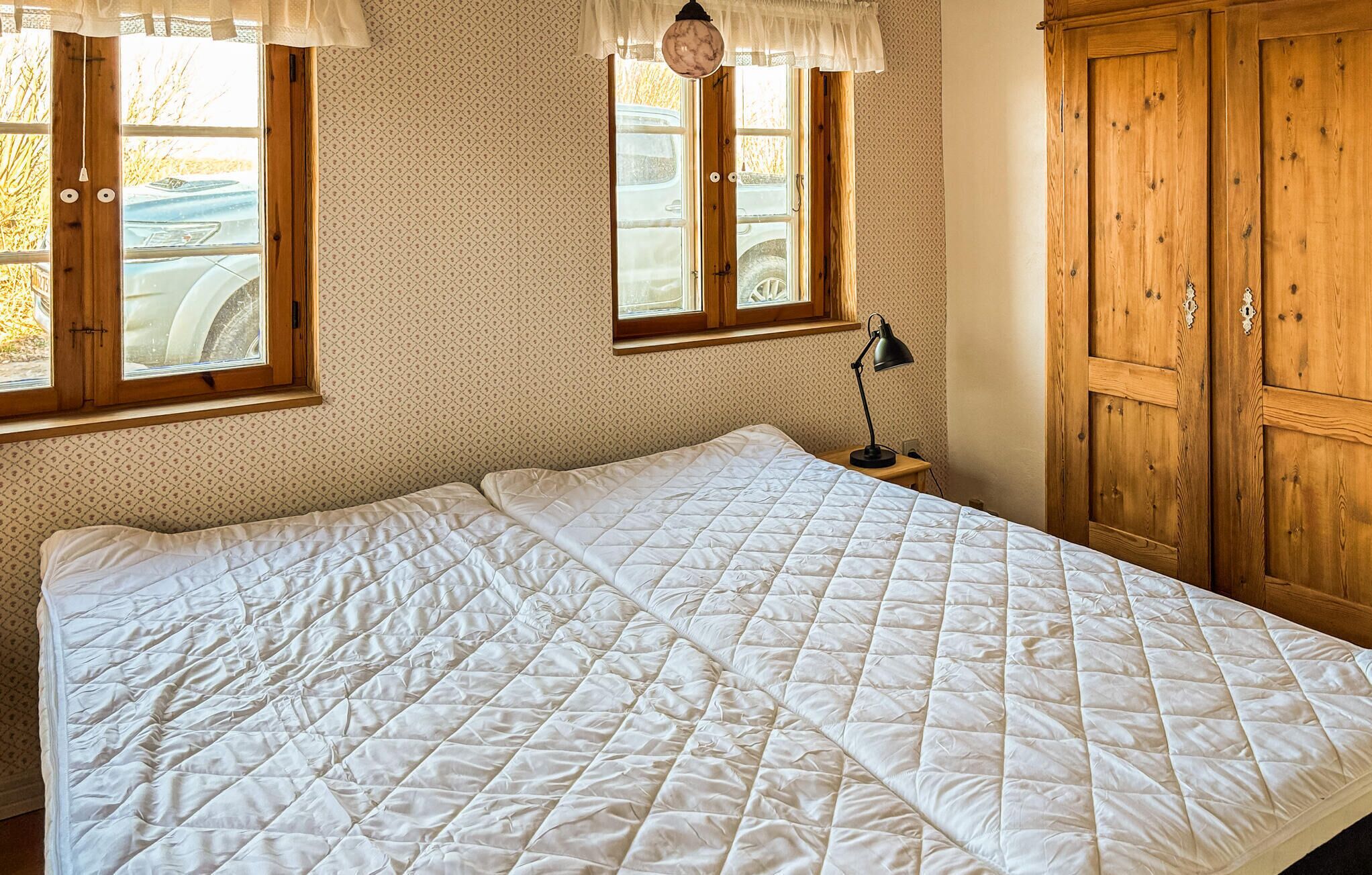 A room with a large bed, wooden wardrobe, and two windows with curtains.