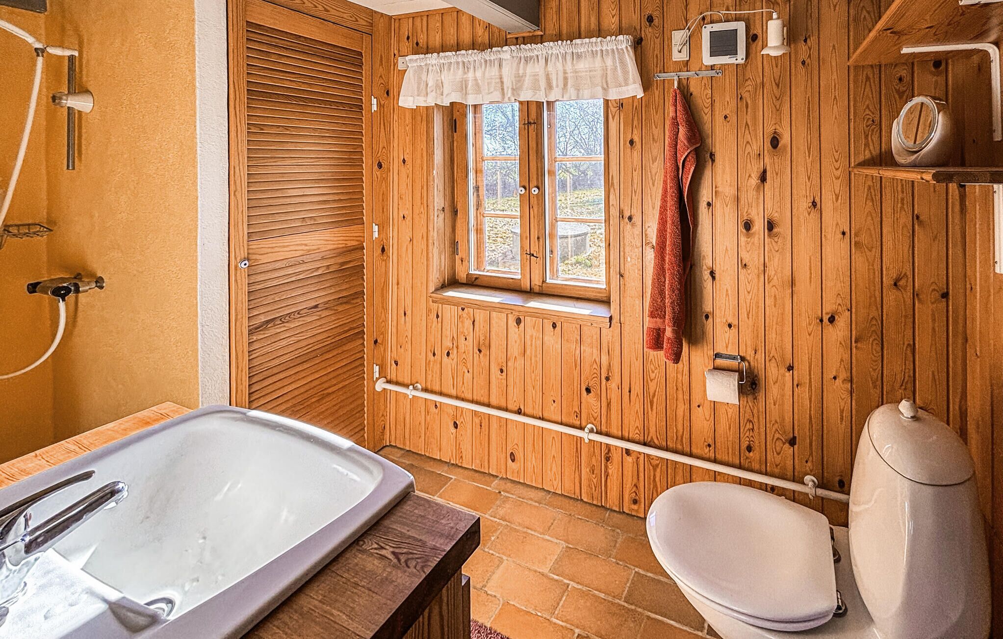 Une salle de bain en bois avec une baignoire, des toilettes et une fenêtre.