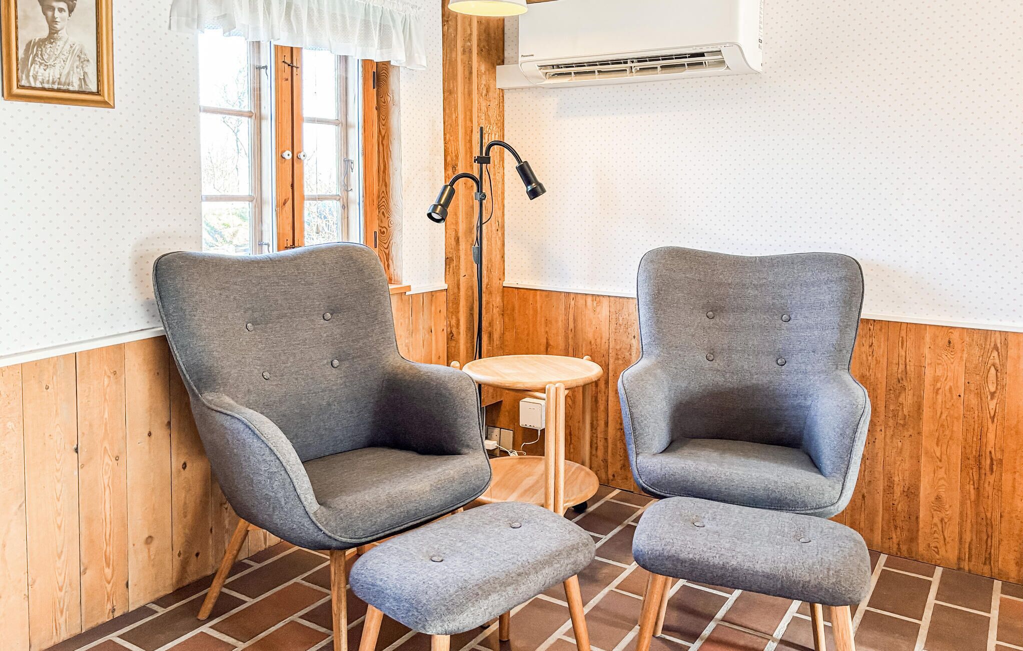 Dos sillones grises tapizados con patas de madera, una pequeña mesa redonda de madera y una unidad de aire acondicionado blanca en la pared.
