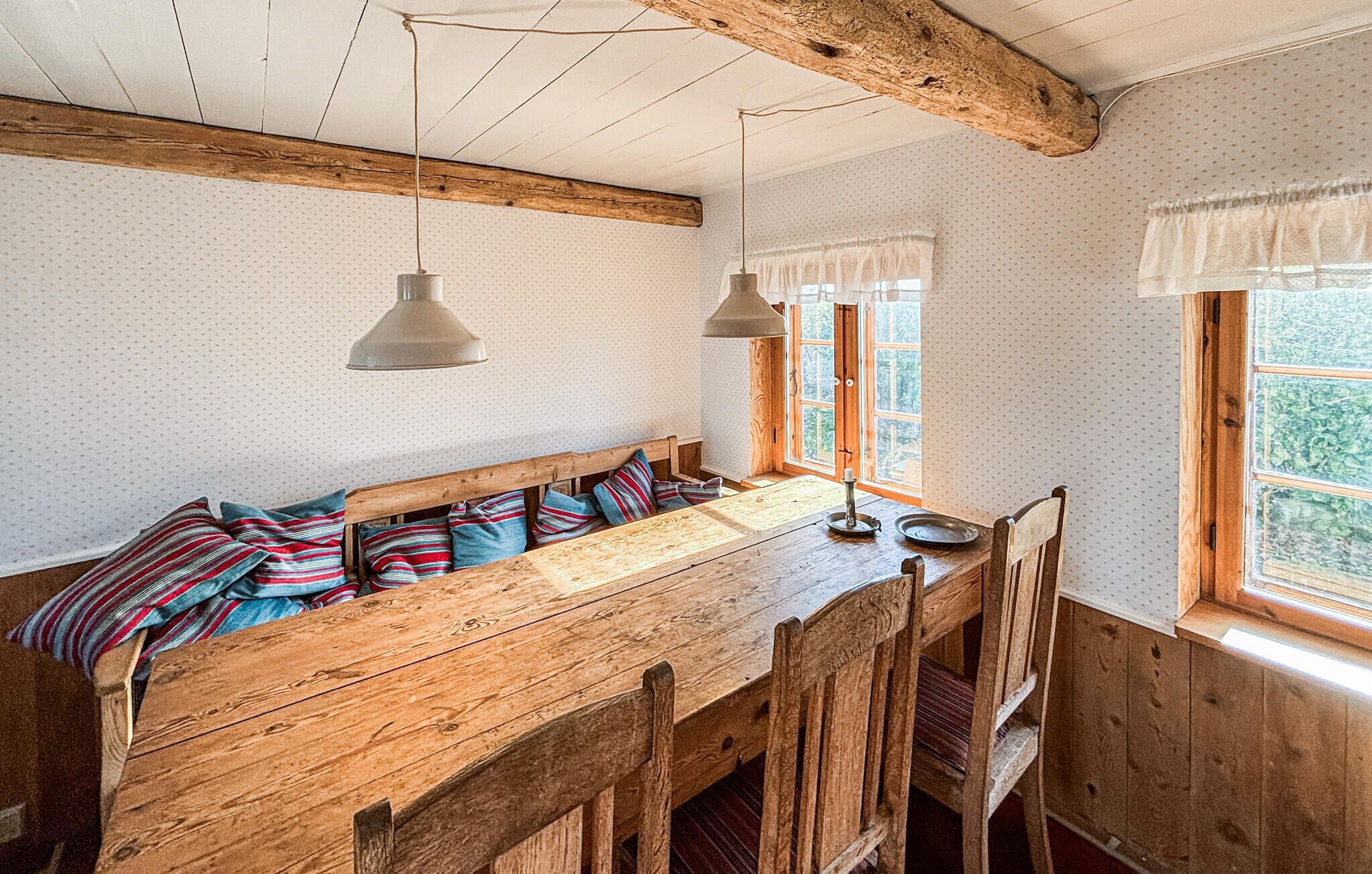 A rustic wooden bench with a bench seat, two pendant lights, and a window with a view of greenery.
