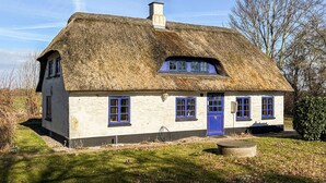 Ein traditionelles reetgedecktes Haus mit einer blauen Tür und Fenstern, umgeben von einer grünen Wiese.