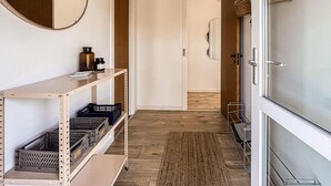 Ein Flur mit Holzboden, einem Metallregal mit Aufbewahrungsbehältern, einem Spiegel und einer Tür.