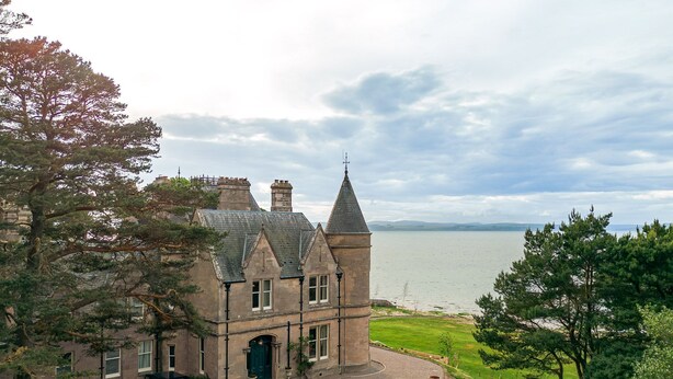 A historic building with a stone facade, a turret, and a view of a lake. - Freya House - Nine Bedroom Villa, Sleeps 18 (Nairn)