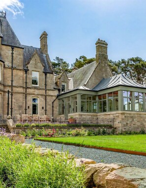 Un grand bâtiment en pierre doté d’un patio couvert et d’un jardin aménagé.