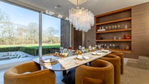 A modern dining room with a large table set for six, surrounded by plush chairs, a chandelier, and a view of the outdoors. - Stardust Mansion - Six Bedroom Villa, Sleeps 12 (Milford)