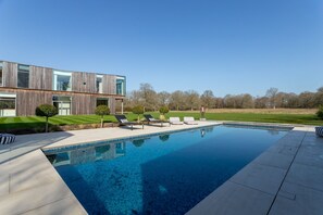 Ein modernes Haus mit Swimmingpool, Liegestühlen und einem gepflegten Rasen.