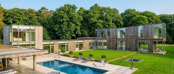 A modern house with a swimming pool, outdoor seating, and a well-maintained lawn.