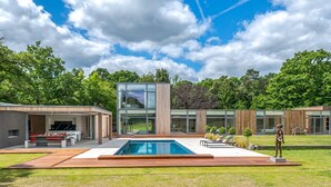 A modern house with a swimming pool, outdoor seating, and a large glass window. - Stardust Mansion - Six Bedroom Villa, Sleeps 12 (Milford)
