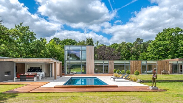 Een modern huis met een zwembad, buiten zitplaatsen en een groot raam.
