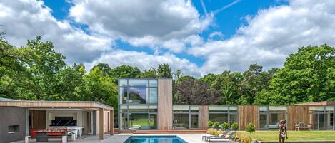 A modern house with a swimming pool, outdoor seating, and a large glass window.