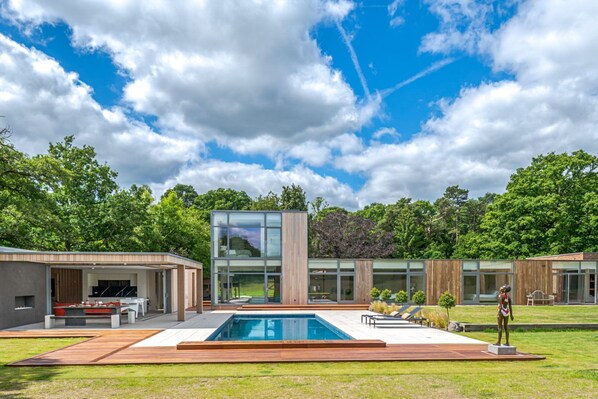A modern house with a swimming pool, outdoor seating, and a large glass window.