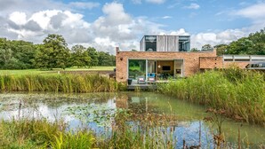 Een modern huis met een grote glazen deur, een bakstenen gevel en een vijver op de voorgrond.