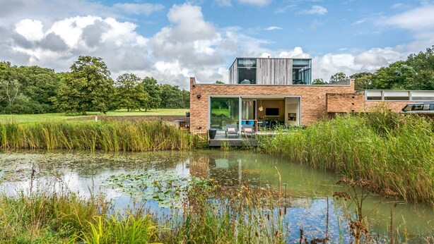 A modern house with a large glass door, a brick exterior, and a pond in the foreground. - Stardust Mansion - Six Bedroom Villa, Sleeps 12 (Milford)
