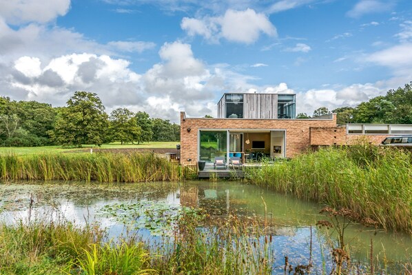 A modern house with a large glass door, a brick exterior, and a pond in the foreground. - Stardust Mansion - Six Bedroom Villa, Sleeps 12 (Milford)