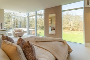 A bedroom with a large bed, a sitting area with a chair, a mirror, and a view of the outdoors. - Stardust Mansion - Six Bedroom Villa, Sleeps 12 (Milford)