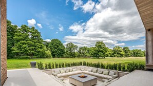Een moderne buiten zithoek met vuurkorf, omgeven door een aangelegde tuin en uitzicht op een grasveld.