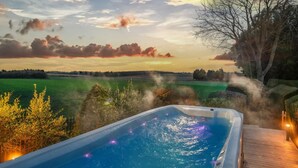 A hot tub with a wooden deck, surrounded by greenery and a view of a field. - Clarence Estate - Eight Bedroom Villa, Sleeps 20 (Woodnesborough)