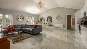 A spacious living room with a grey sectional sofa, a chandelier, and a dining area with a white table and chairs. - Clarence Estate - Eight Bedroom Villa, Sleeps 20 (Woodnesborough)